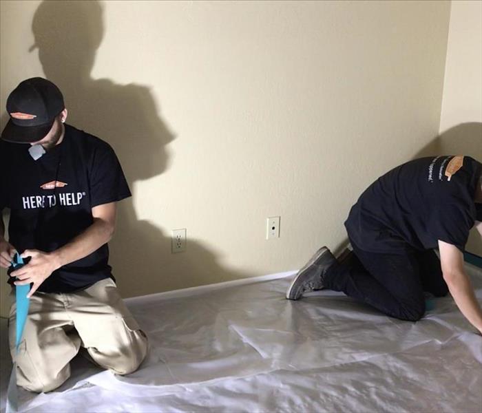 Two SERVPRO technicians lay out plastic sheeting to catch drywall debris