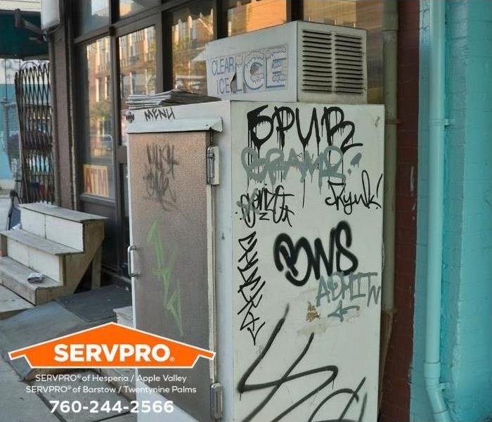 The side of an outdoor cooler is defaced by graffiti.